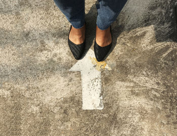 Low section of woman standing by arrow sign on road