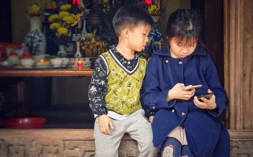 Boy sitting with sister using smart phone on railing