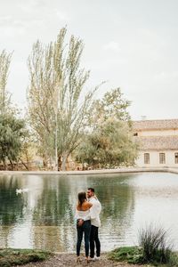 Rear view of couple standing by lake against trees