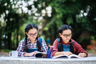 Friends reading book while sitting against trees