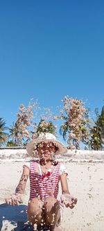 Side view of woman sitting on beach against clear blue sky