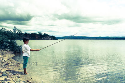 Rear view of man fishing at sea shore against sky