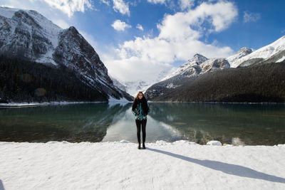 Woman standing at lakeshore against snowcapped mountain