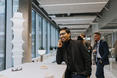 Smiling young businessman talking on mobile phone during conference