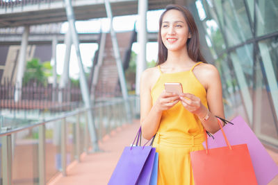 Smiling young woman using mobile phone while standing outdoors