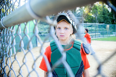 Portrait of girl standing at playing field seen through chainlink fence