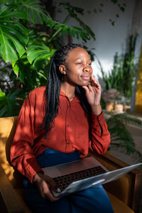 Thoughtful relaxed black woman take break from laptop look aside window dreaming, enjoy sun on face