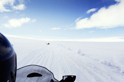 Cropped image of person riding snowmobile on landscape against sky