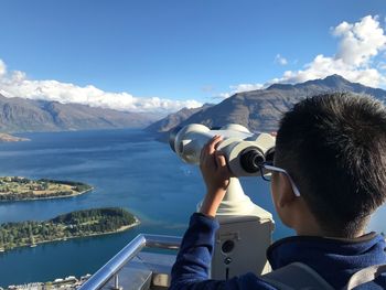 Rear view of boy looking through coin-operated binoculars against valley