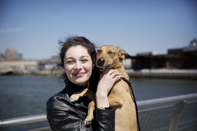 Portrait of happy woman with dog standing on footbridge against sky