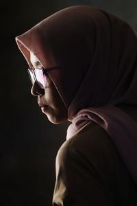 Woman in headscarf looking away against black background