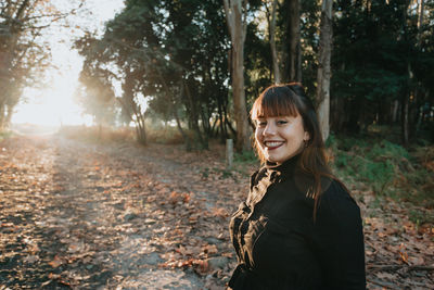 Portrait of young woman standing against trees