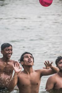 Shirtless men playing with ball in sea