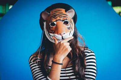 Portrait of woman wearing tiger mask against blue wall
