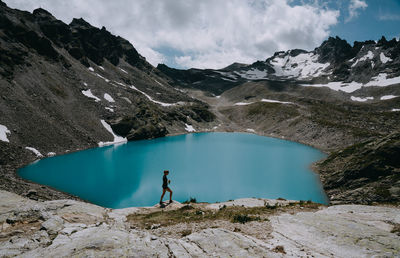 Full length of woman standing by lake and mountains against sky