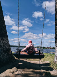 Rear view of cute girl sitting on swing against sky