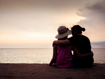 Rear view of couple on beach against sky during sunset