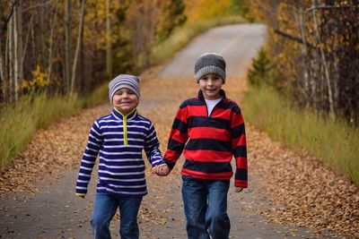 Portrait of brothers holding hands while walking on road amidst autumn trees