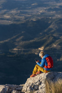 Young woman standing on rocks on top of a mountain with mobile phone.