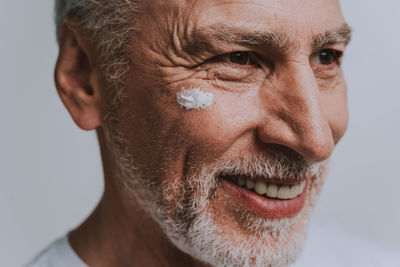 Close-up of smiling senior man with moisturizer on face against white background
