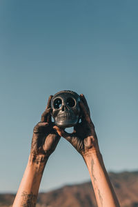 Female hands holding a black pottery skull into the air against a blue sky.