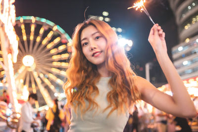 Portrait of young woman holding illuminated sparklers at night