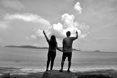 Rear view of men standing on beach against sky