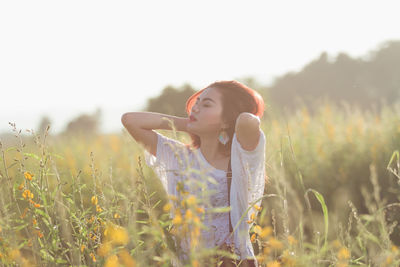 Woman with hand in hair standing against sky