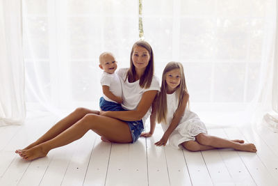 Mother with daughter and son sitting on a white wooden floor in a large room