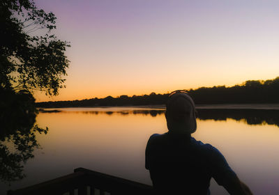 Rear view of silhouette man looking at lake against sky during sunset