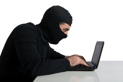 Woman using laptop while sitting on sofa against white background