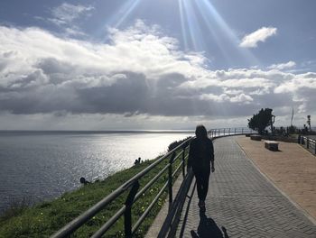 Rear view of man walking by sea against sky