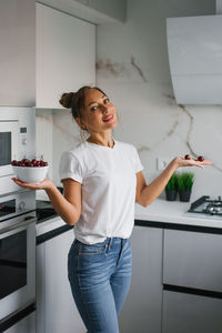 Pretty girl in a white t-shirt is standing in the kitchen and holding a white vase with red