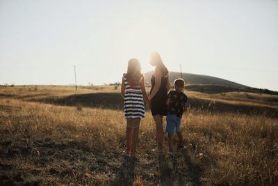 Rear view of people standing on grass against sky