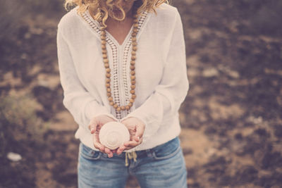 Midsection of mature woman holding seashell while standing on field