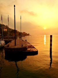 Wooden posts in sea against sky during sunset