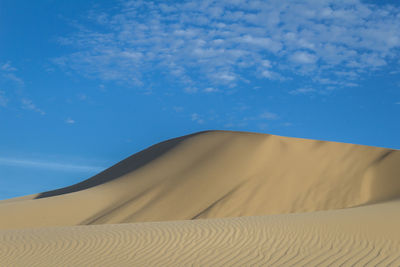 Low angle view of sand dunes against blue sky