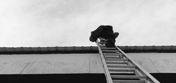 Low angle view of man standing on roof against sky