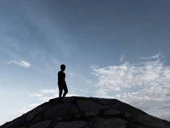 Low angle view of man standing on rock against sky