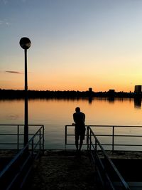 Silhouette man standing on railing by lake against clear sky