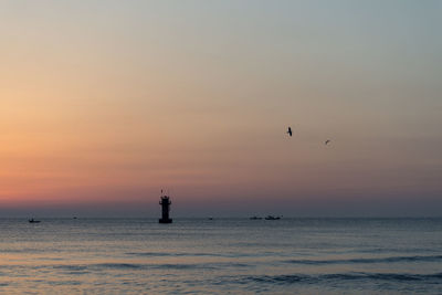 Silhouette bird flying over sea against sky during sunset