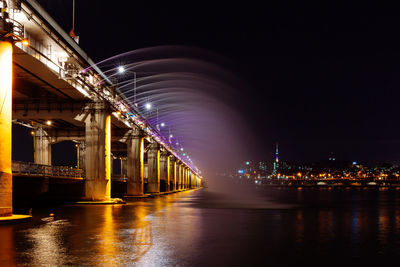 Low angle view of illuminated bridge over river at night