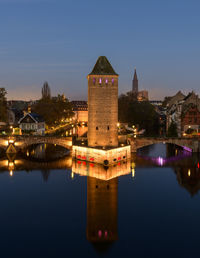 Illuminated buildings by river against sky at night