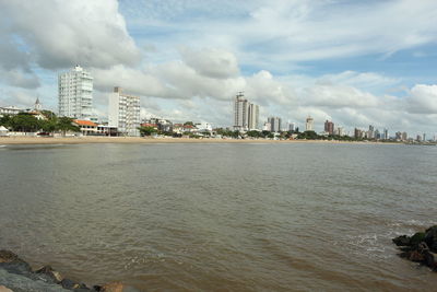 City at waterfront against cloudy sky