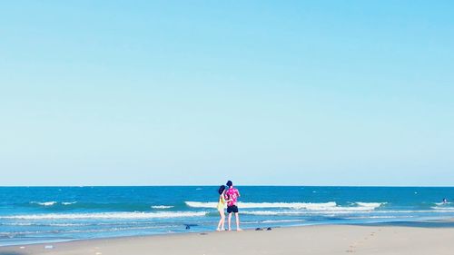 Rear view of boys on beach against clear sky