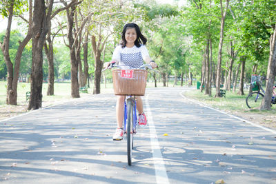 Portrait of woman riding bicycle on road against trees