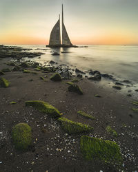 Sailboat on sea shore against sky during sunset