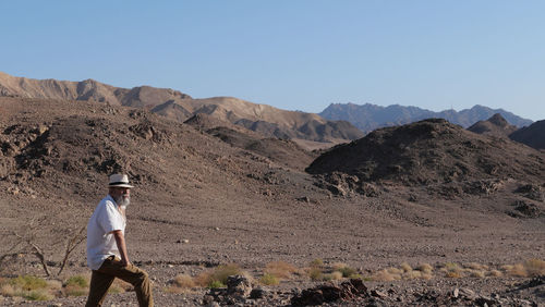 Senior man standing on mountain against clear sky