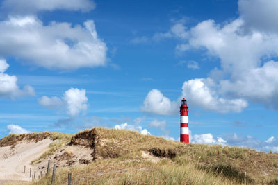 Lighthouse on field against cloudy sky