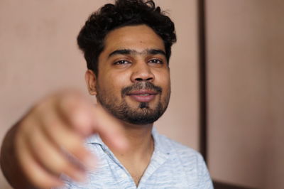 Portrait of smiling young man pointing against wall